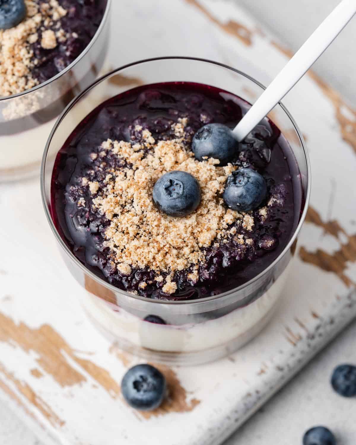 a cup with no bake cheesecake topped with blueberry sauce and spoon in cup.