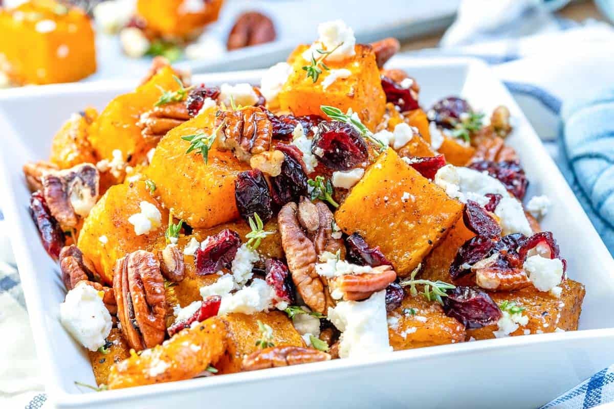 roasted butternut squash in a bowl topped with pecans and feta cheese.