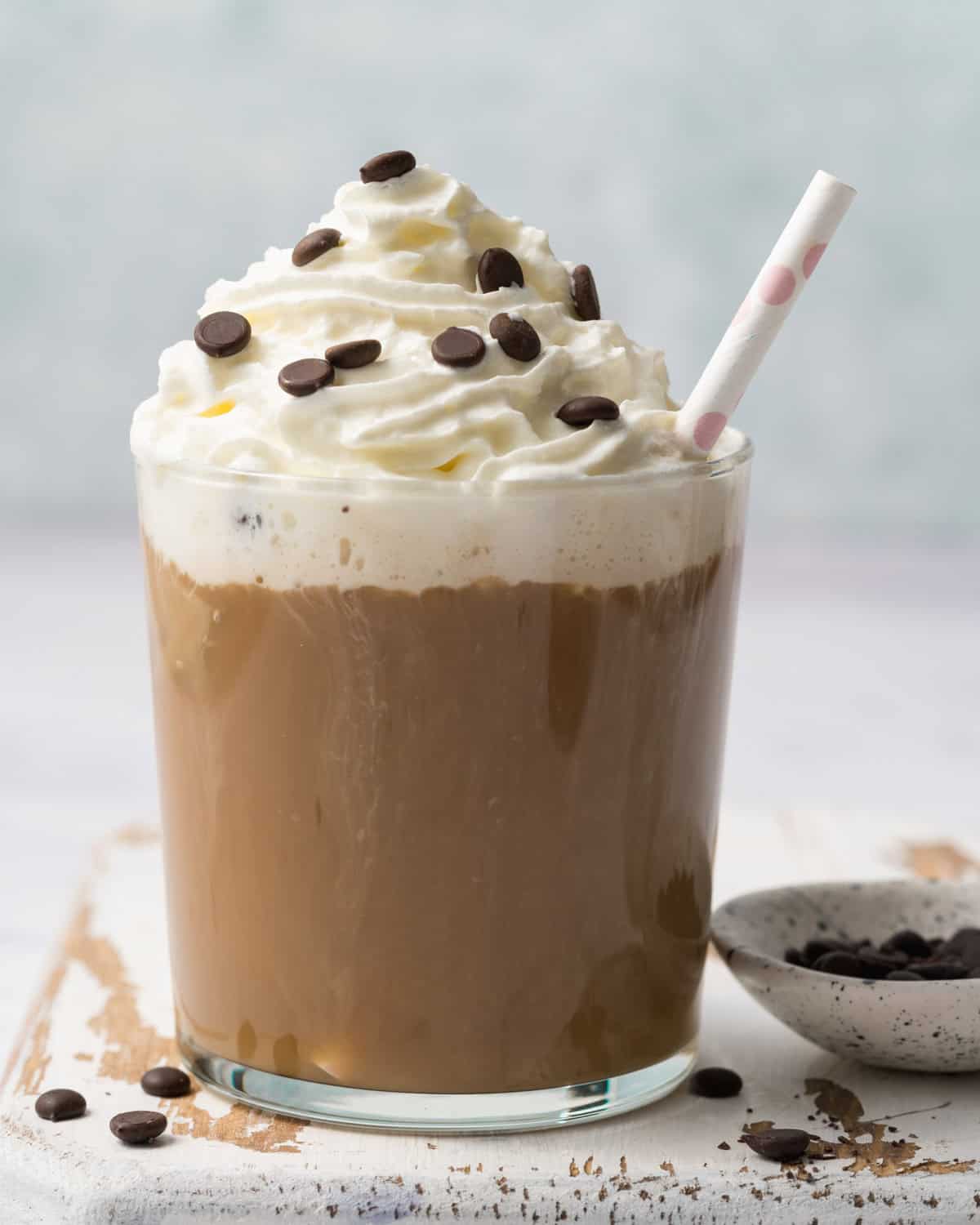 a mocha brown looking protein smoothie in a glass cup topped with whip cream and chocolate chips.