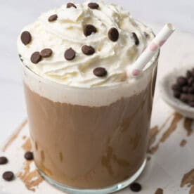 a glass cup with mocha smoothie topped with whip cream and chocolate chips.