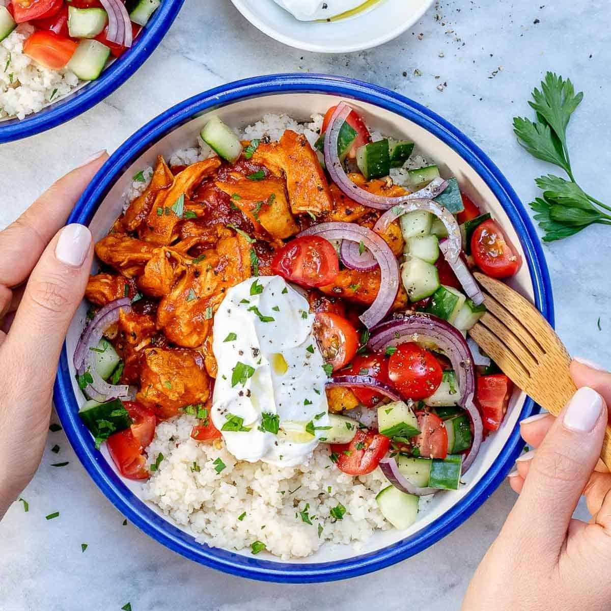 a hand holding a bowl with moroccan chicken, with couscous, and salad.