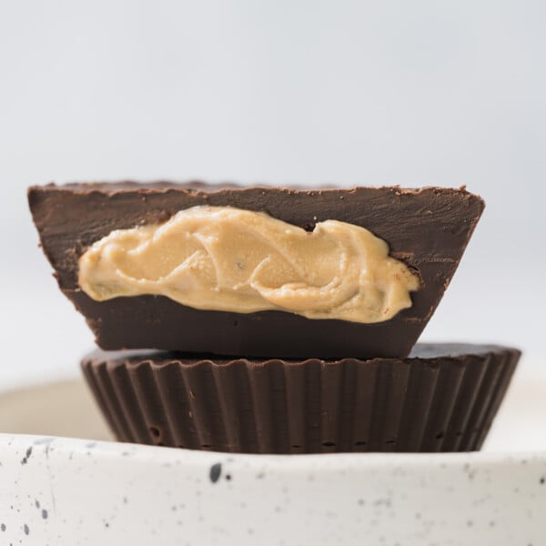 two peanut butter cups on a plate with one sliced in half showing the middle of it.