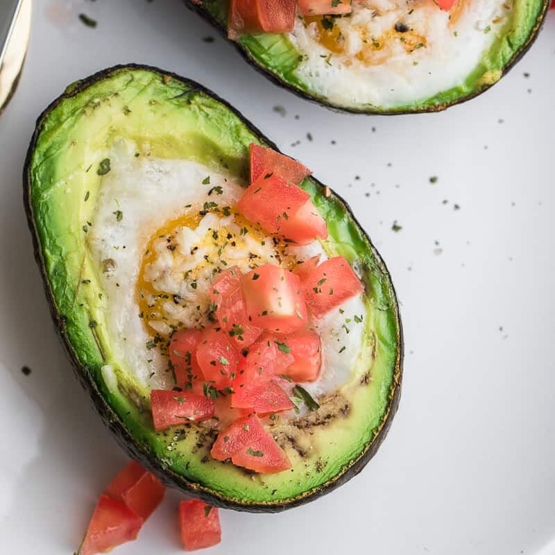 half an avocado with a baked egg in it topped with chopped tomatoes.