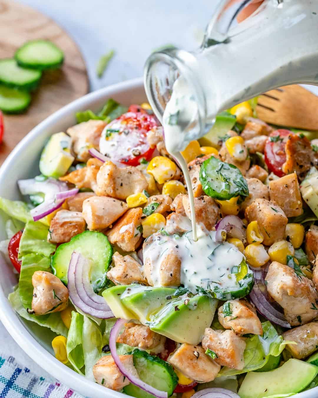 homemade ranch dressing being poured over chicken salad in a dish.