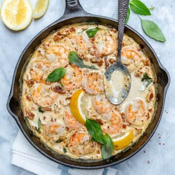 top view of Tuscan shrimp in a creamy sauce in black skillet with metal spoon in skillet and on top left there are 2 lemon wedges next to the skillet
