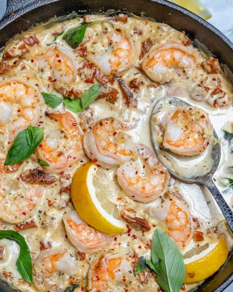 top view of creamy shrimp with lemon and basil garnish  in a black skillet with metal spoon in skillet