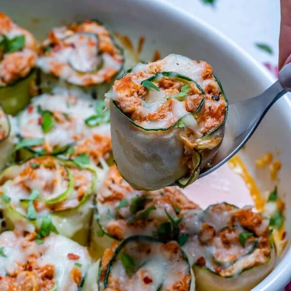 chicken enchilada roll up with zucchini on a spoon over a white casserole dish