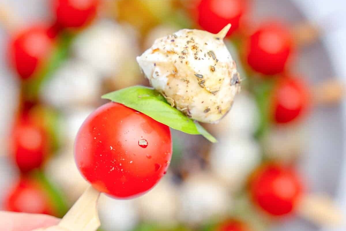 Hand holding a single caprese skewer.