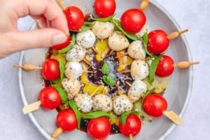 adding seasoning to the caprese skewers on a plate.