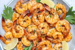 broiled shrimp served on a plate with lemon wedges.