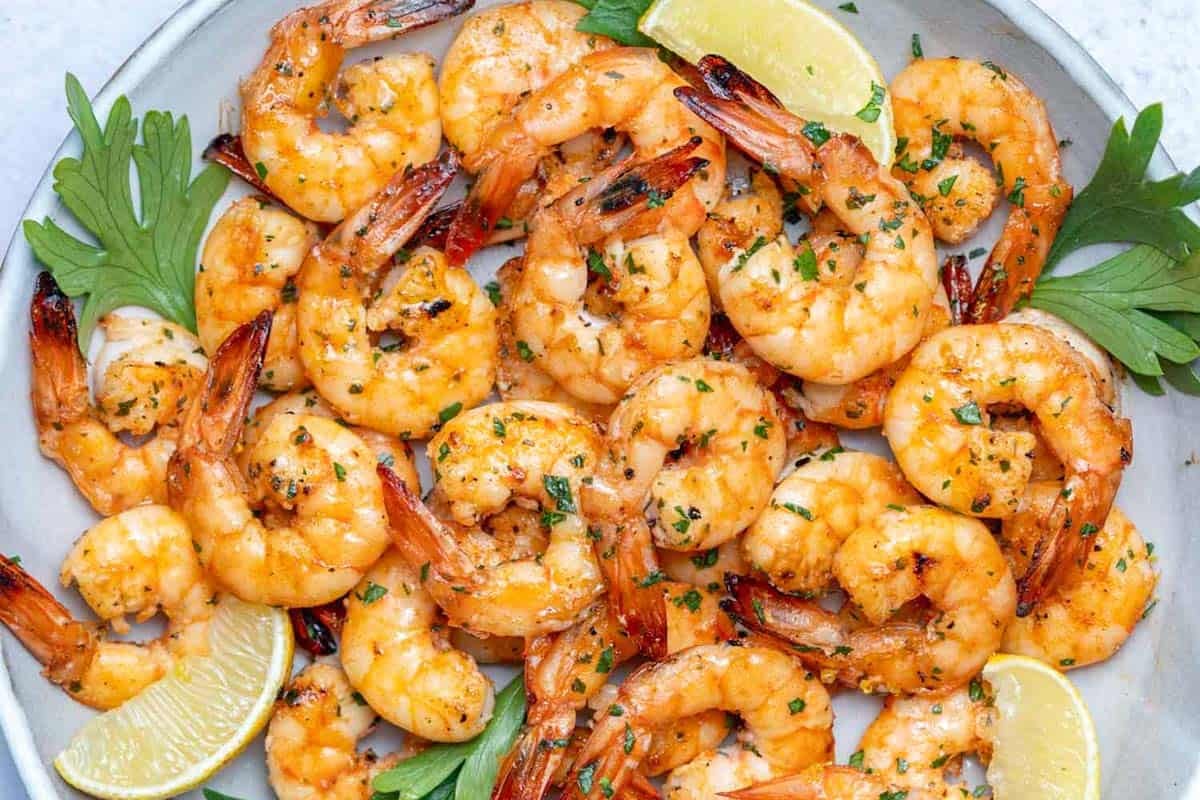 broiled shrimp served on a plate with lemon wedges.
