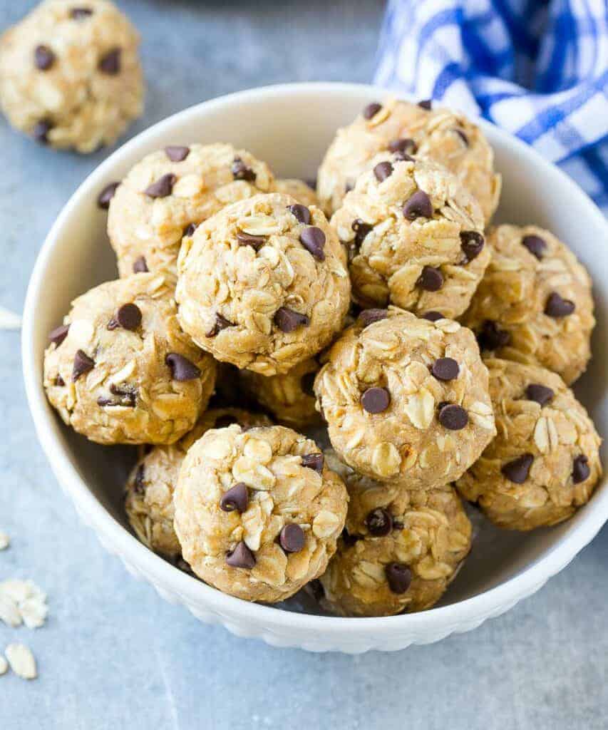 top view of a white bowl with energy balls made with oats, peanut butter, and chocolate chip next to a kitchen towel that is white and blue