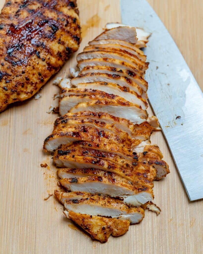 sliced grilled chicken  on a cutting board with a knife next to it 