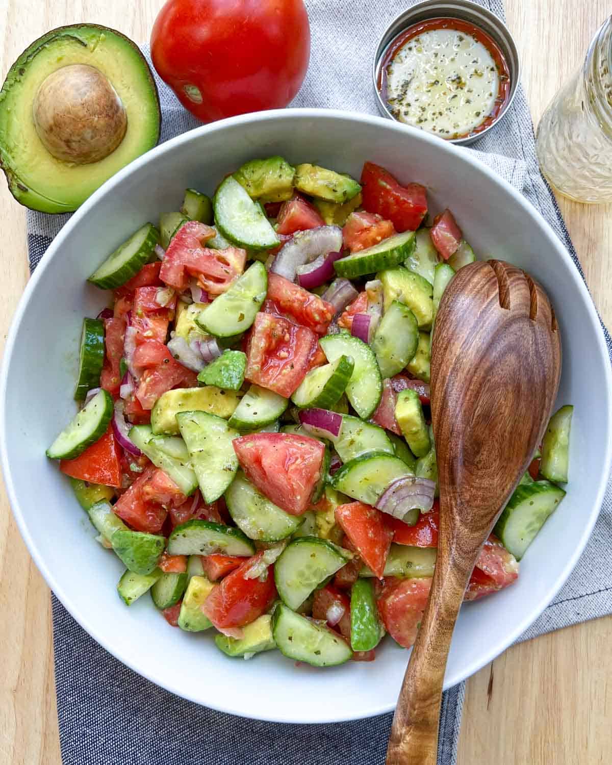 white dish with salad and wooden spoon in salad on the right side.