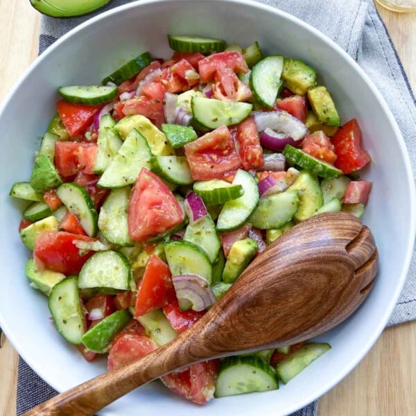 Avocado tomato salad in a bowl with a wooden spoon in a bowl.