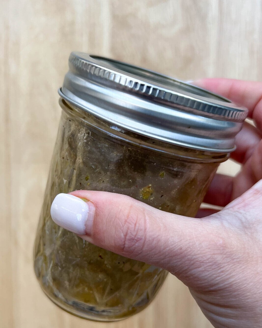 Salad dressing ingredients mixed in a mason jar. Hand-holding jar.