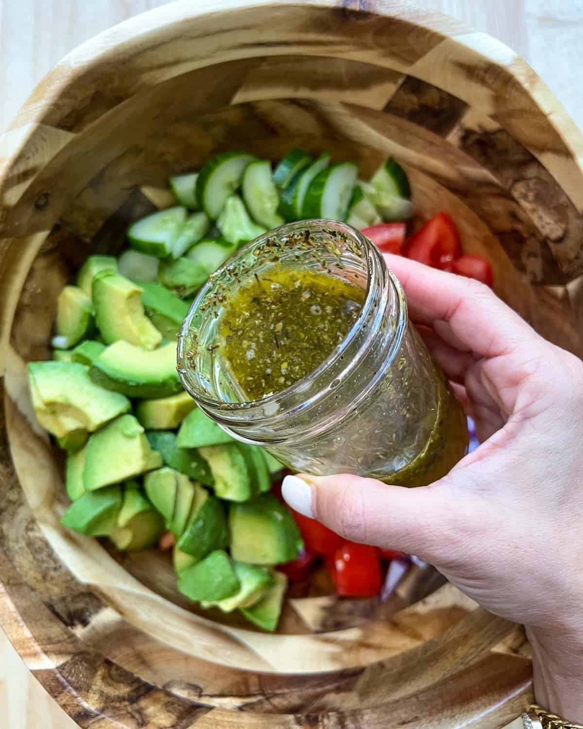 Hand-holding mason jar with salad dressing, pouring it.