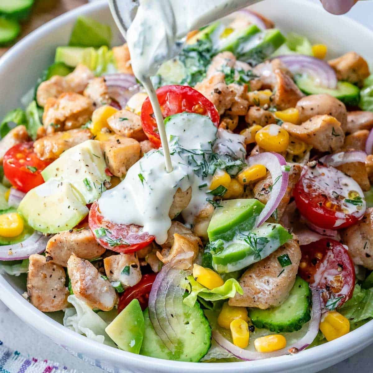 pouring ranch over the salad in a bowl.