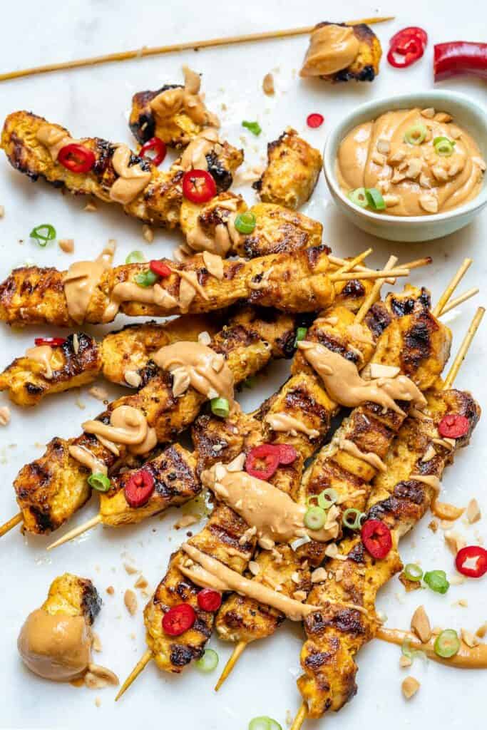 top view of chicken satay skewers on a flat surface with peanut dipping sauce