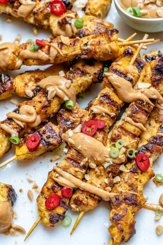 thai chicken skewers on a flat surface with peanut sauce drizzled all over it 