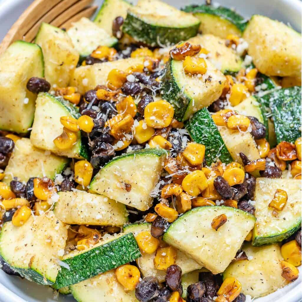 close up image of grilled corn and chopped zucchini and beans, topped with shaved parmesan cheese