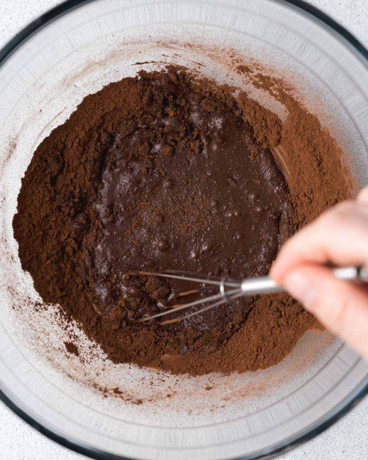 hand holding whisk and mixing cocoa powder and milk to form a paste.