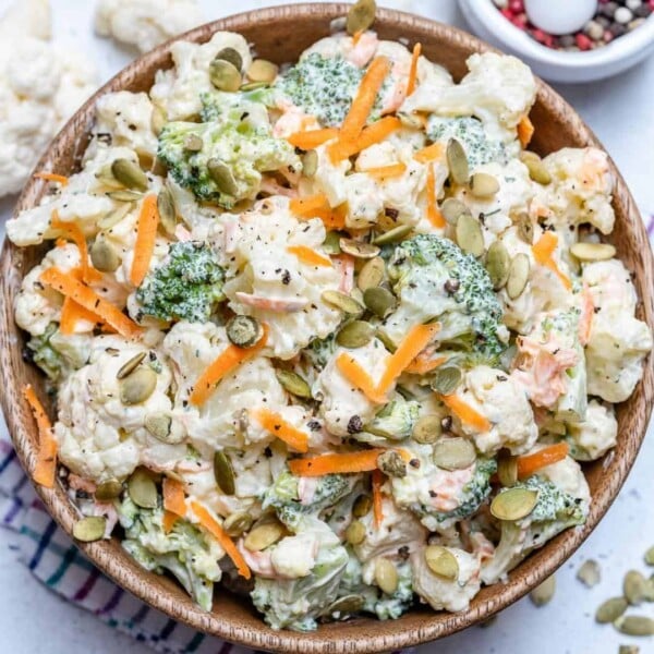 a round bowl with creamy cauliflower and broccoli salad topped with shredded carrots and pumpkin seeds.