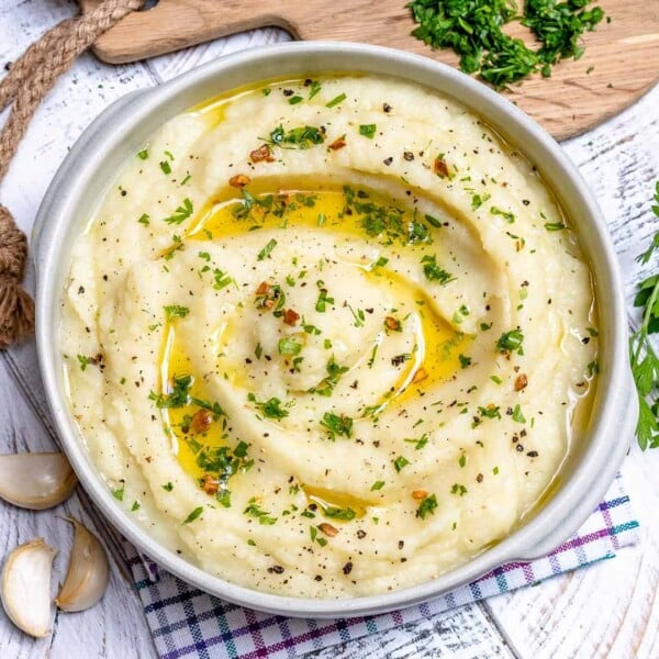 a round bowl with Garlic butter mashed cauliflower topped with melted butter and fresh herbs.