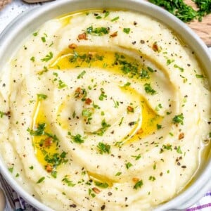 a round white bowl with cauliflower mash that is topped with melted butter and fresh herbs.