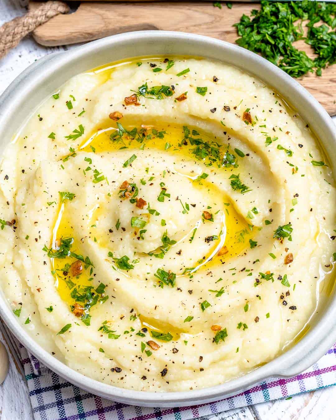 a round white bowl with cauliflower mash that is topped with melted butter and fresh herbs