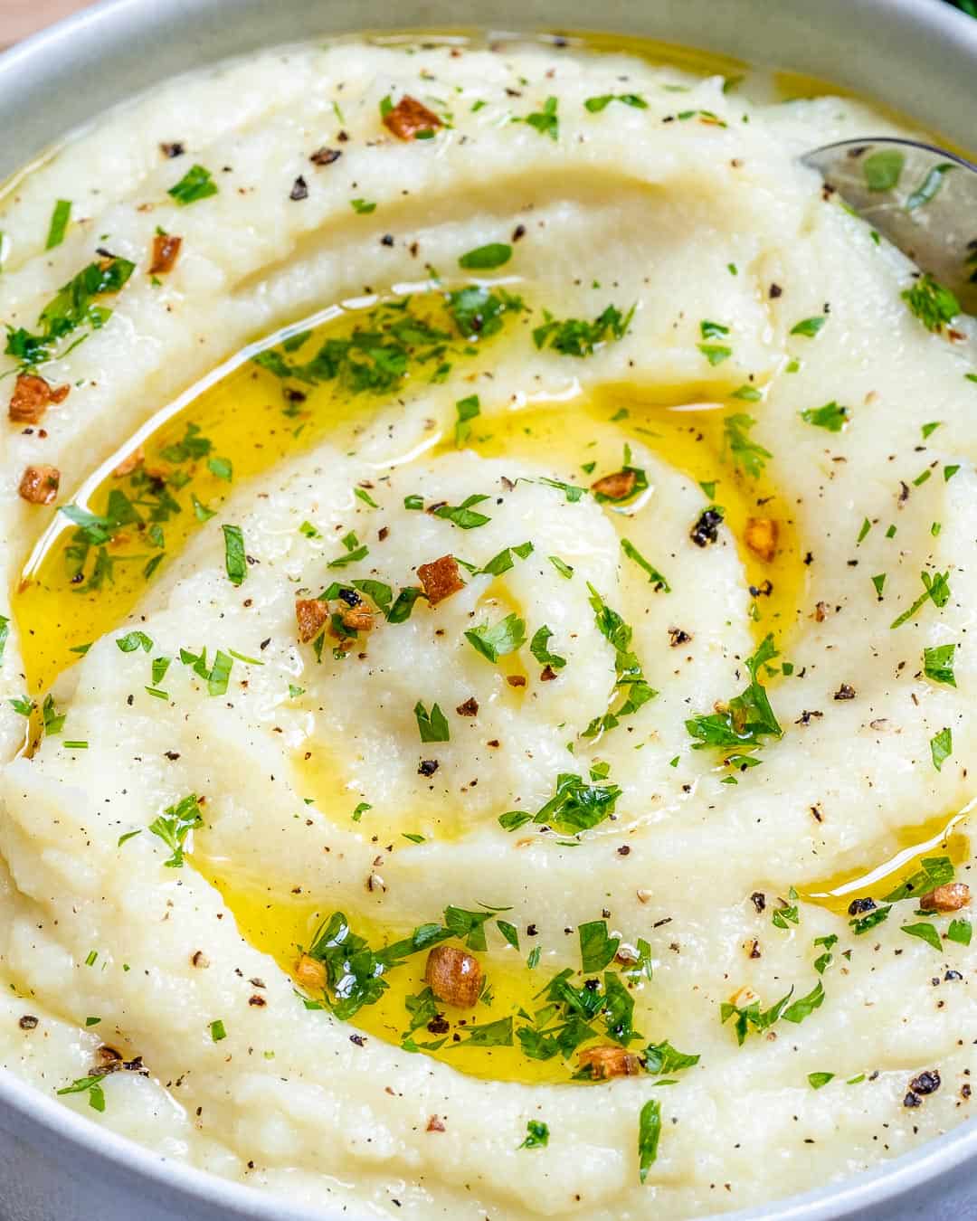 mashed cauliflower in a bowl topped with melted butter and fresh garlic