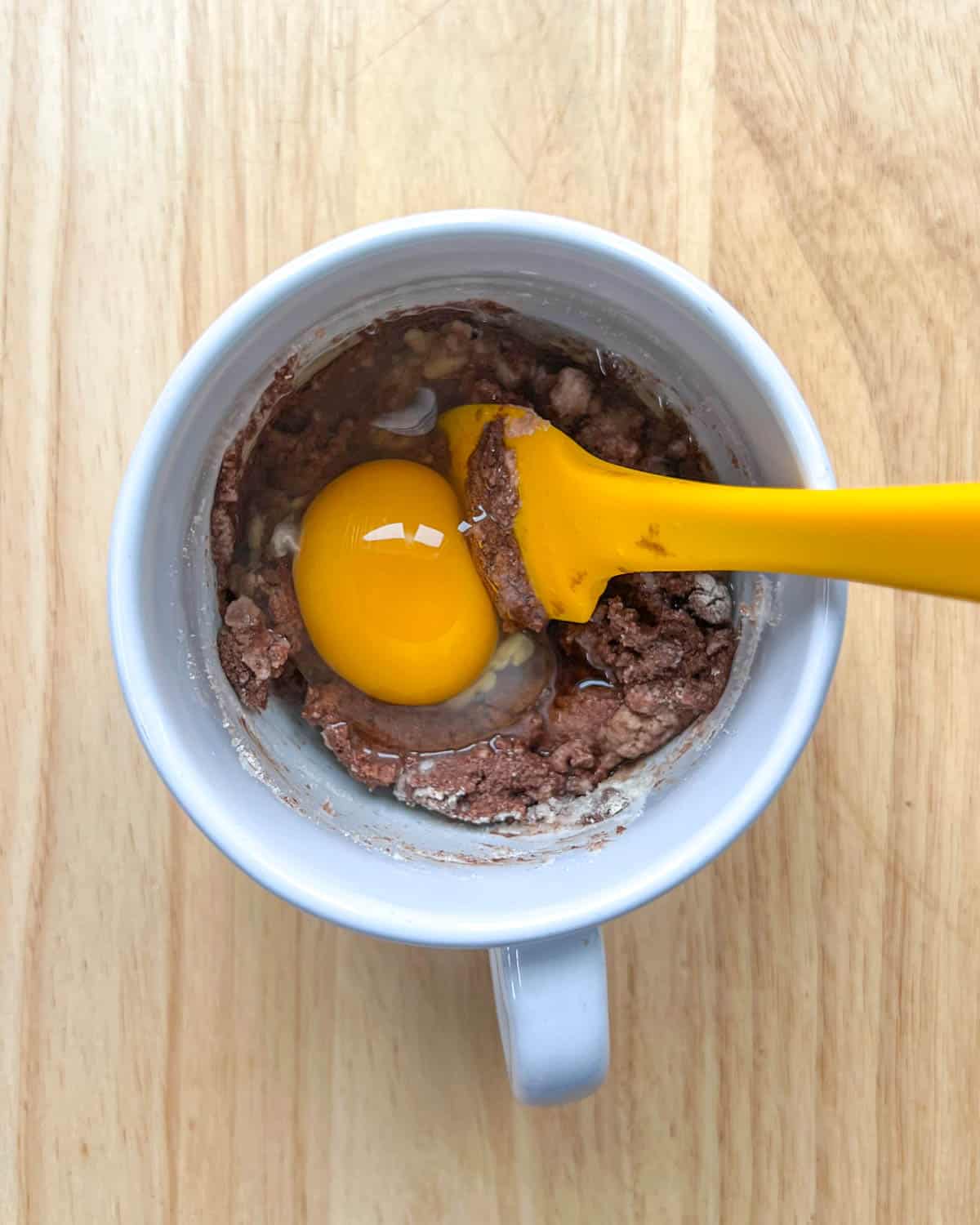 one egg added over the chocolate and flour mixture in a white cup.