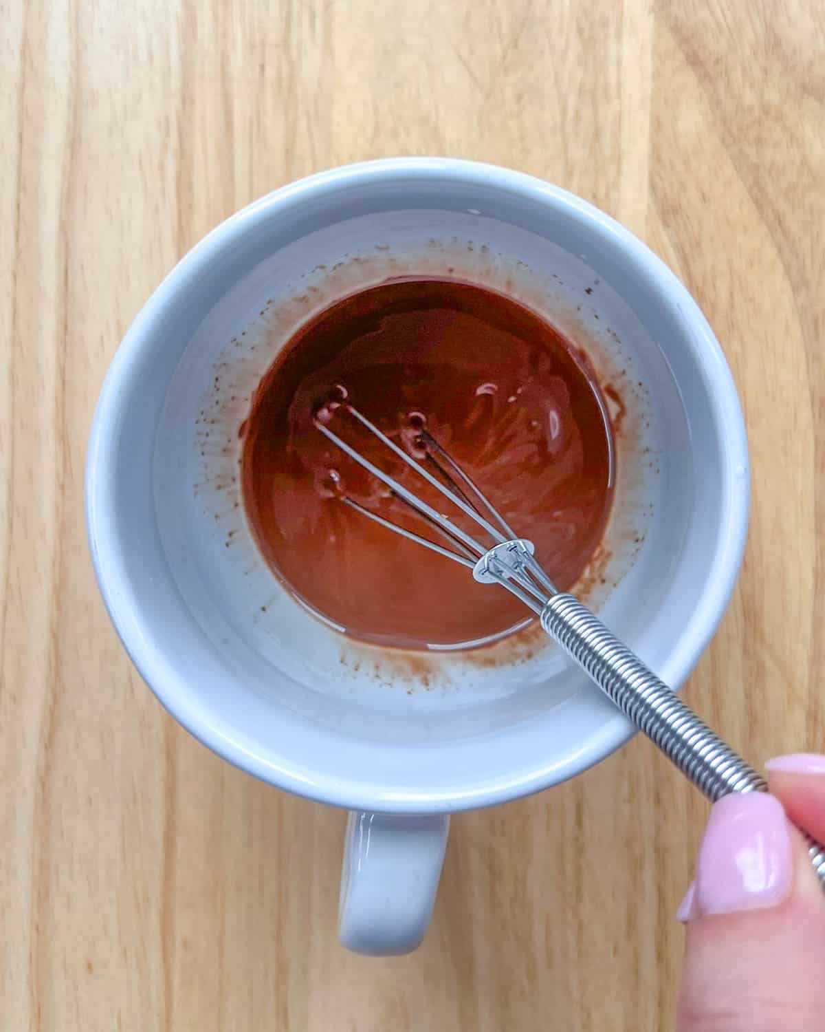 melted chocolate in a white cup with whisk in the cup.