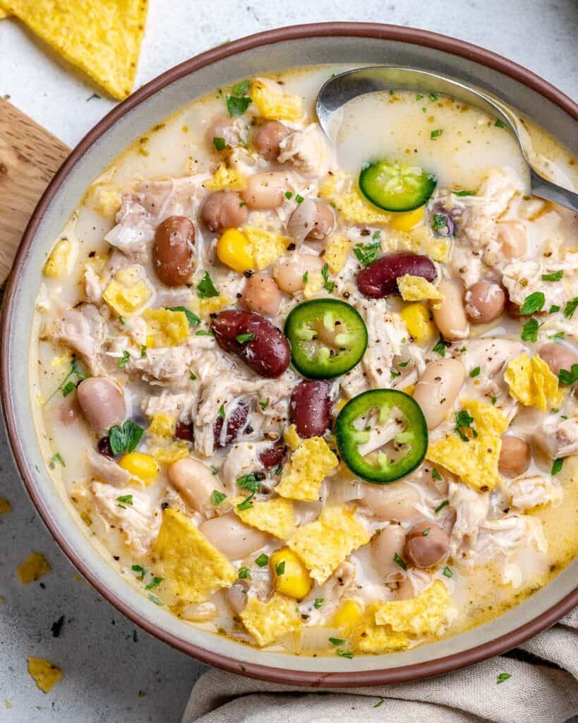 top view of a bowl with white chicken chili and 3 types of beans topped with sliced jalapenos