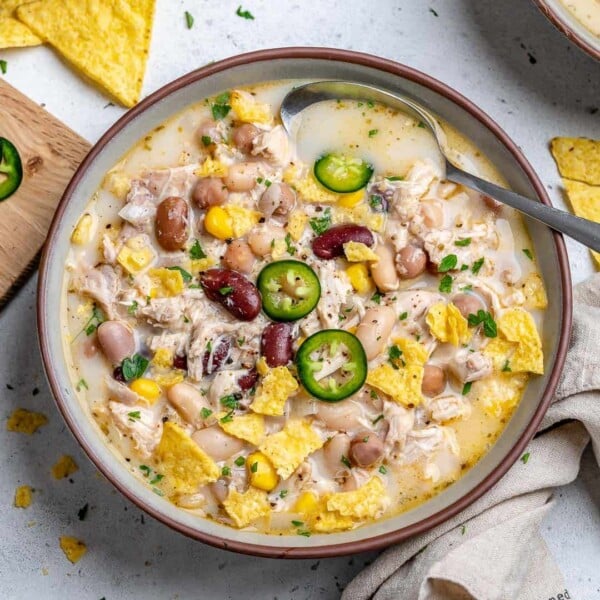 A round bowl with white chicken chili made with four different beans garnished with sliced jalapenos.