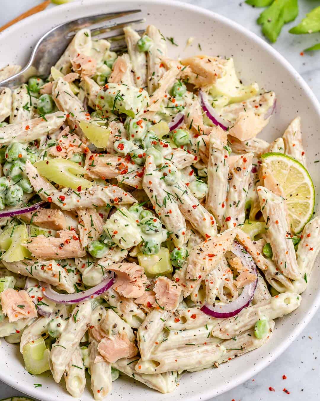 a round dish with a creamy tuna pasta salad topped with fresh dill garnish and lime wedge.