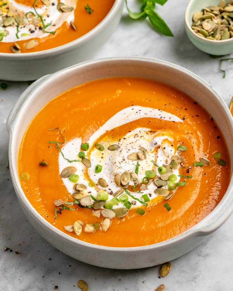 side shot of vegetarian  pumpkin soup in a white bowl topped with sour cream