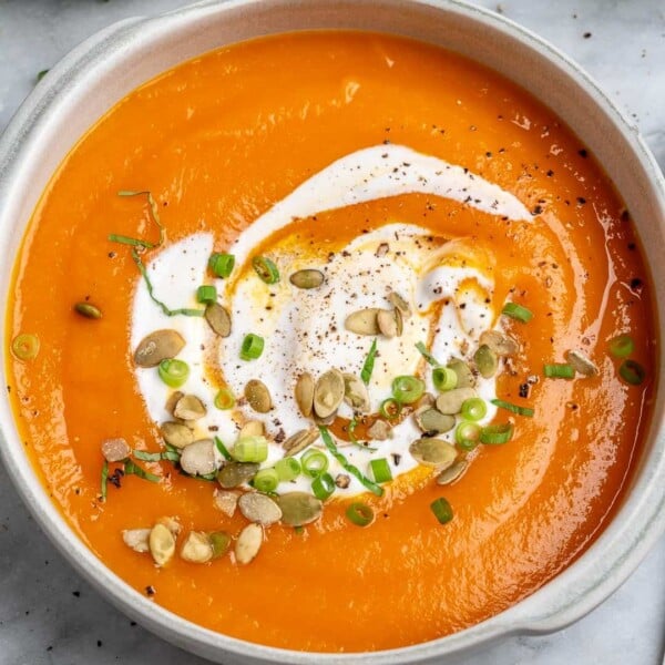 pumpkin soup in a round white bowl topped with yogurt and pumpkin seeds.