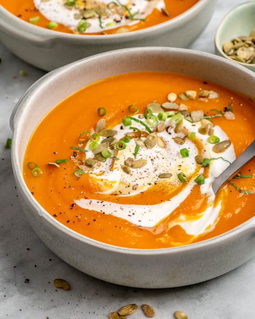 carrot and pumpkin soup in a white bowl topped with cream and pumpkin seeds