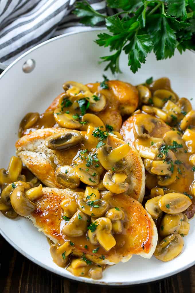  sauteed chicken breasts topped with mushroom sauce over a white skillet 