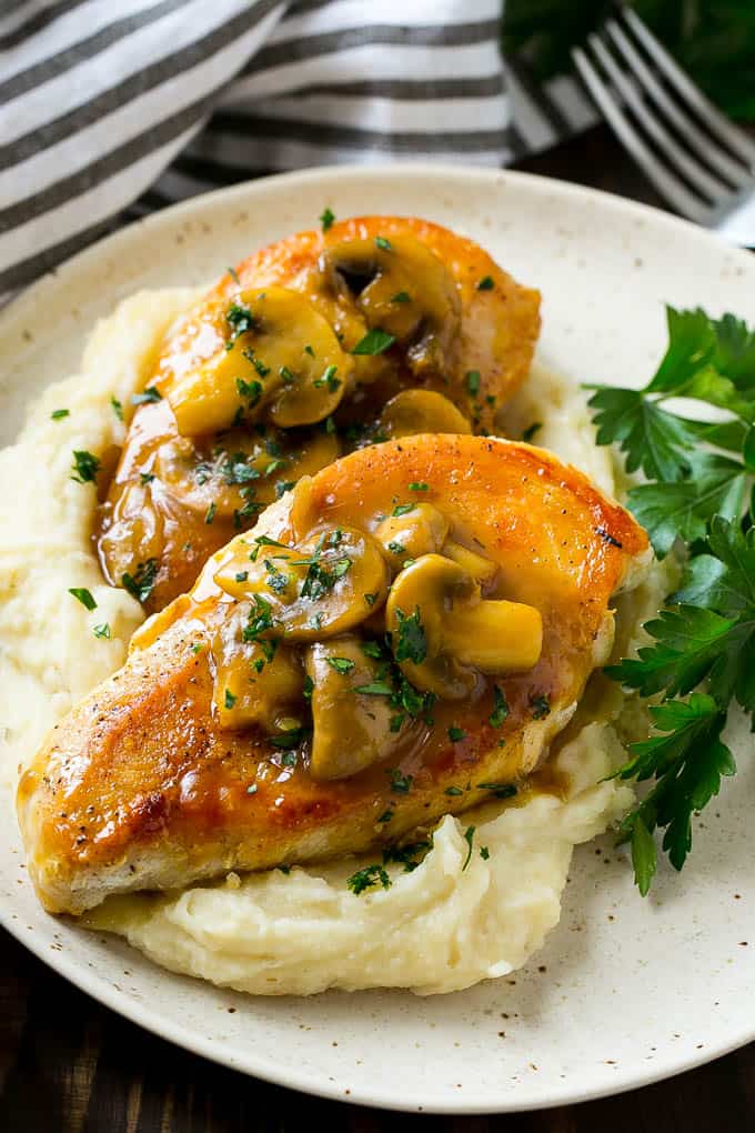 chicken marsala topped with mushrooms over a plate of mash potatoes 