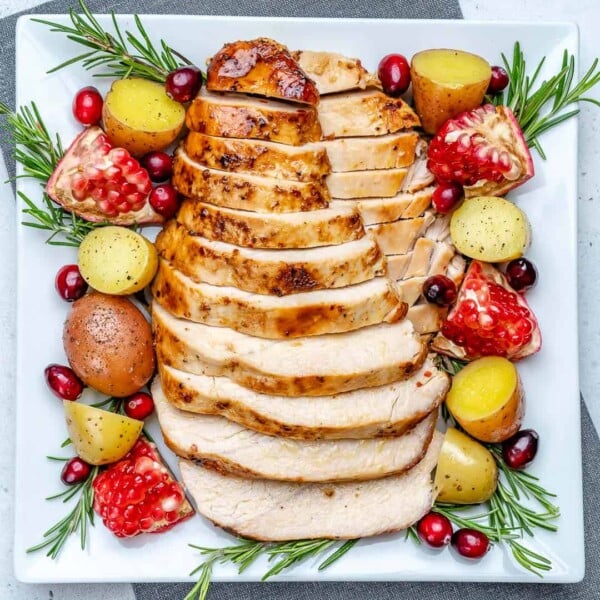 top view of sliced turkey breasts on a white plate with baby potatoes fresh rosemary and pomegranates