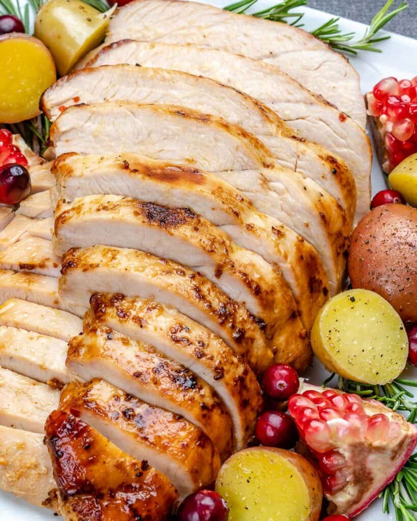 Close up of sliced cooked turkey breast with baby potatoes and fresh pomegranate arils to the side of it