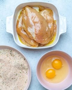 chicken marinated in a bowl, bread crumbs in another bowl, two eggs in a third bowl.