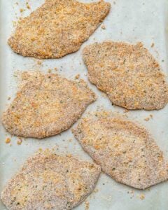 breaded chicken cutlets before baking, placed on a sheetpan.