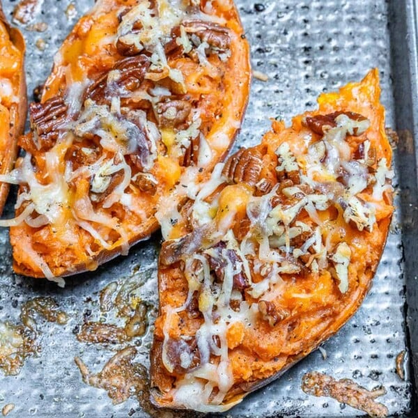 2 twice baked sweet potatoes on a sheet pan topped with chopped pecans and melted cheese.