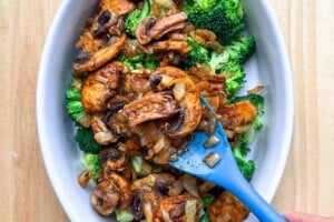 arranging the sauteed mushrooms over the broccoli in a dish.