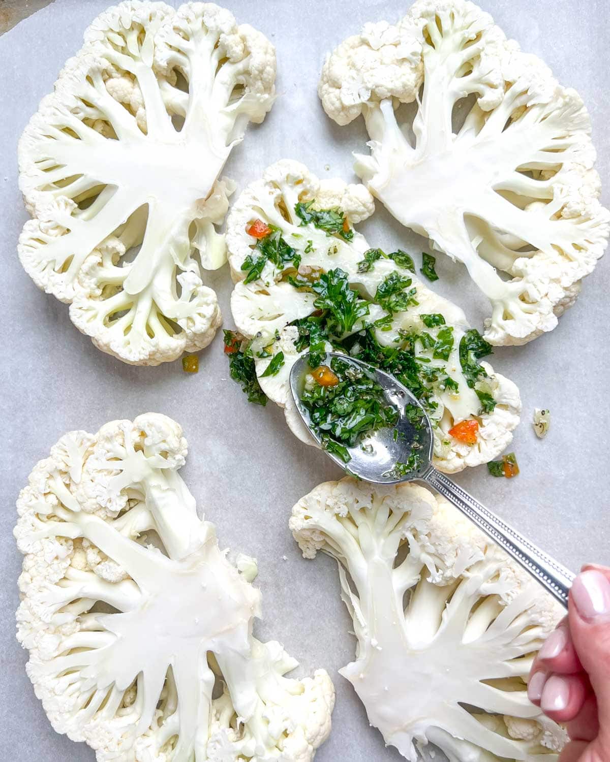 hand with a spoon adding chimichurri sauce over cauliflower steaks.