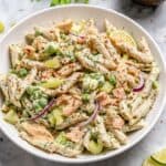 a white round bowl with tuna pasta salad that it garnished with fresh chopped dill and lime wedges.