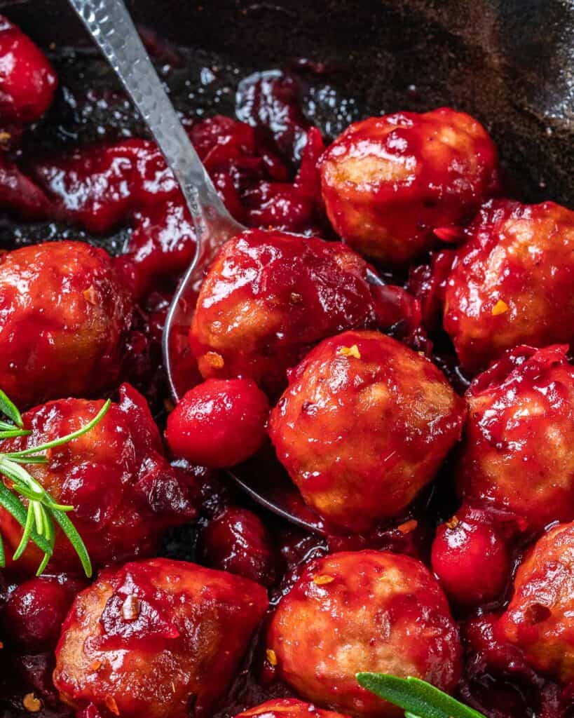 spoon grabbing 2 drenched chicken meatball with cranberry sauce